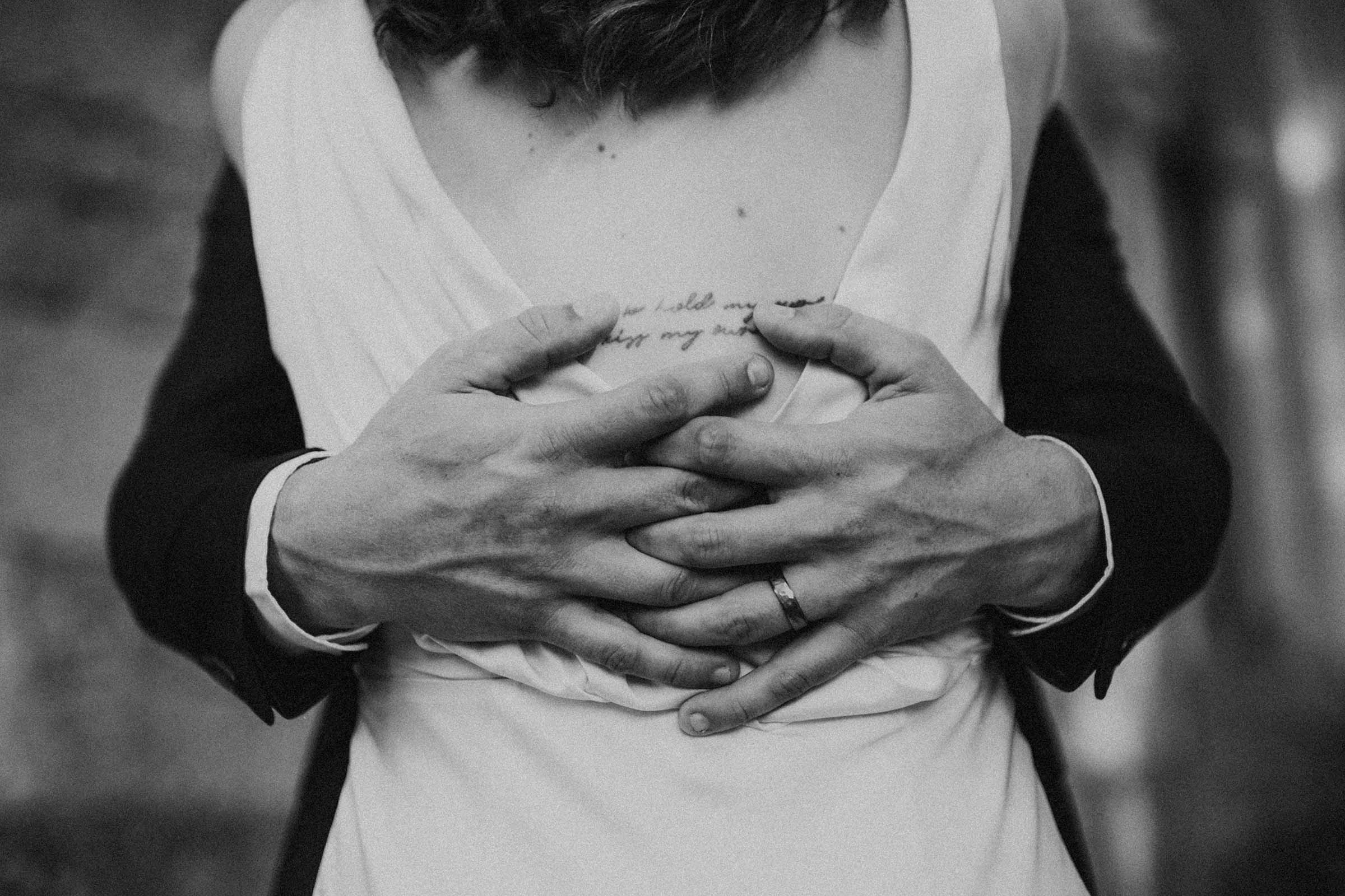 black and white hands holding behind brides back with tattoo written